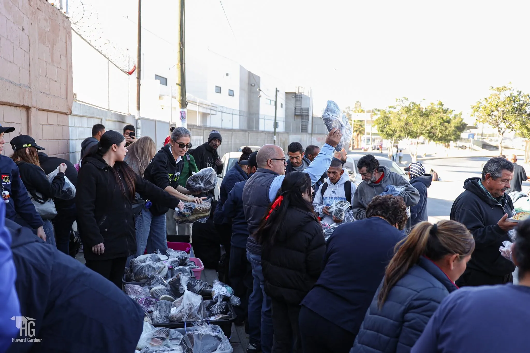 Personas reunidas en la calle reciben bolsas con calzado y ropa durante la entrega de El Zapatón